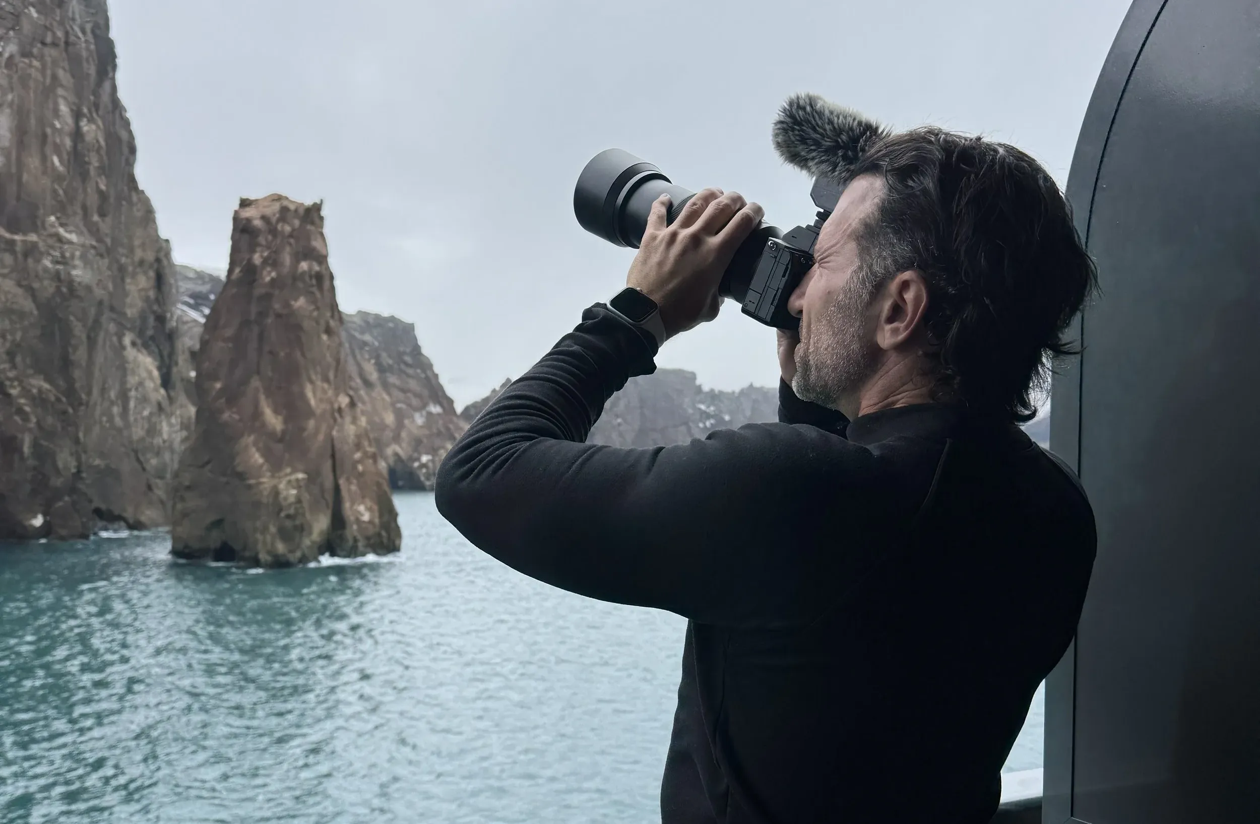 Phil Lockwood points a camera upward while sailing through Deception Island, Antarctica
