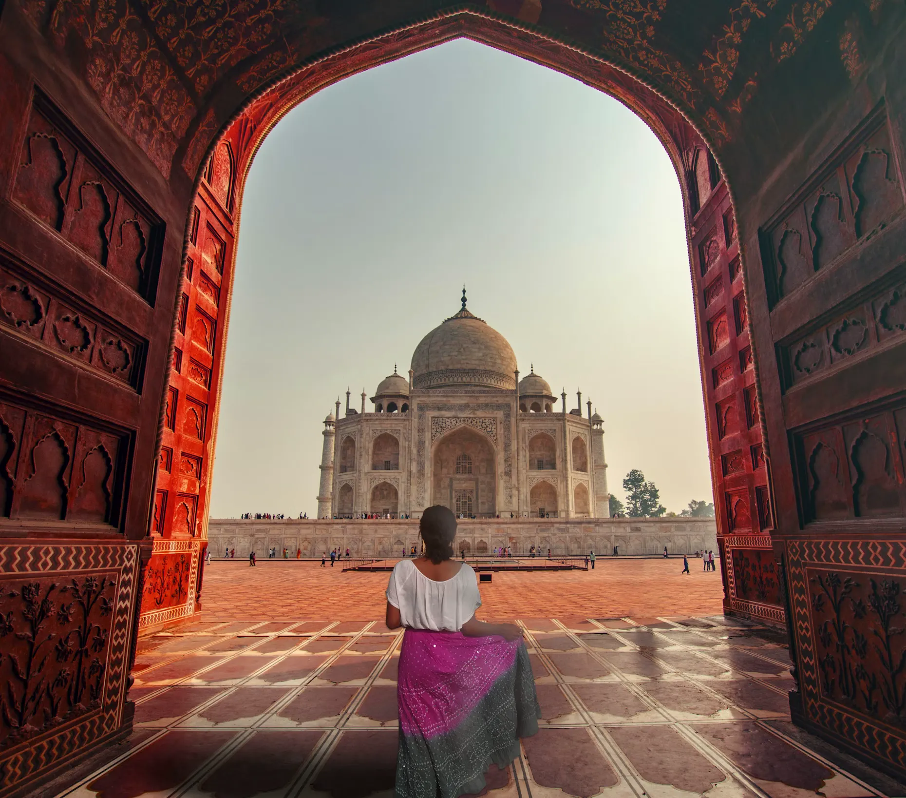 A woman stands under an arch with the Taj Mahal in the background