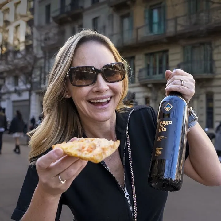 Erin Lockwood holds up a bottle of wine and a piece of food in Barcelona