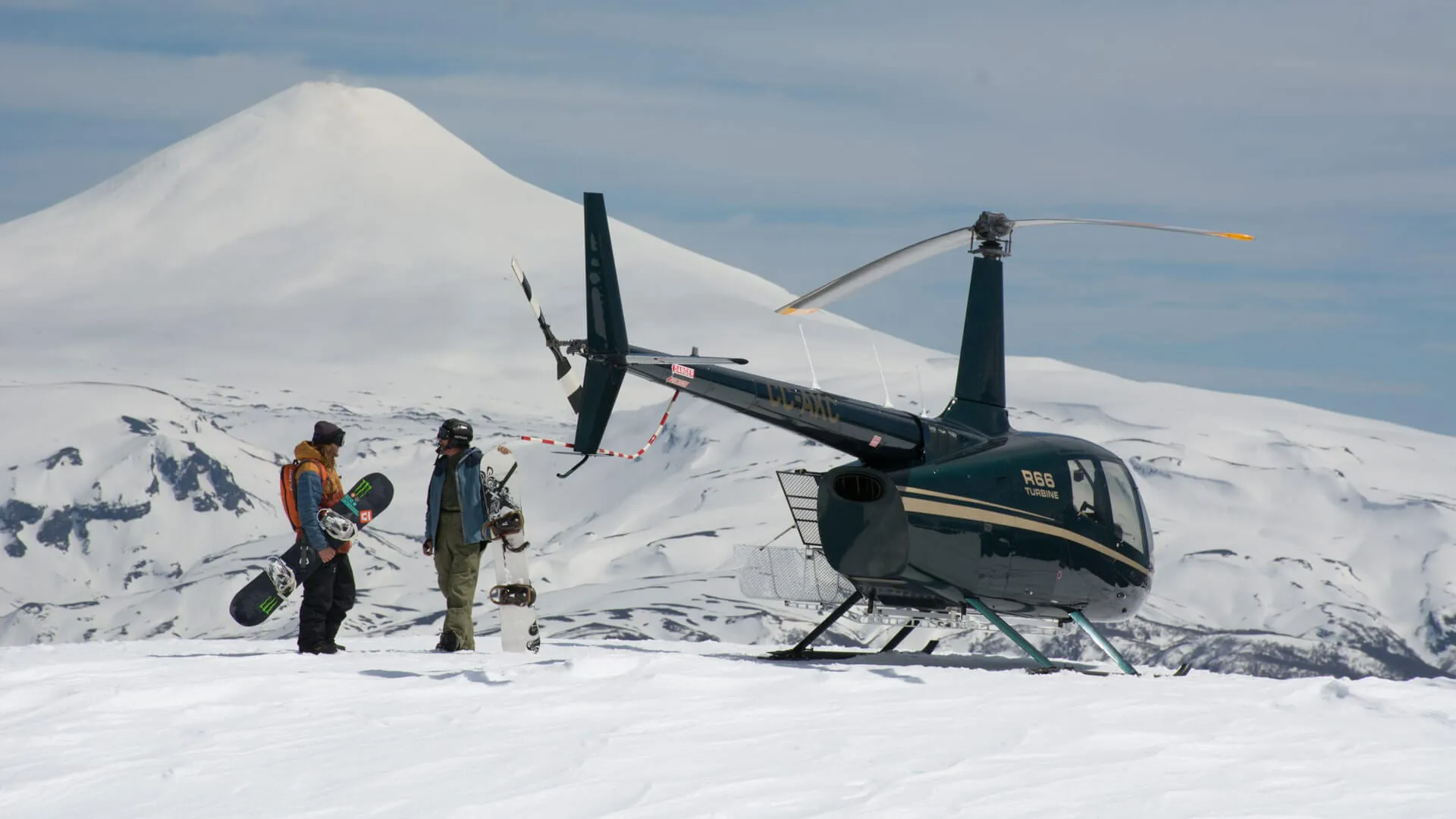 A helicopter sits on a snowy mountain with skiers close by
