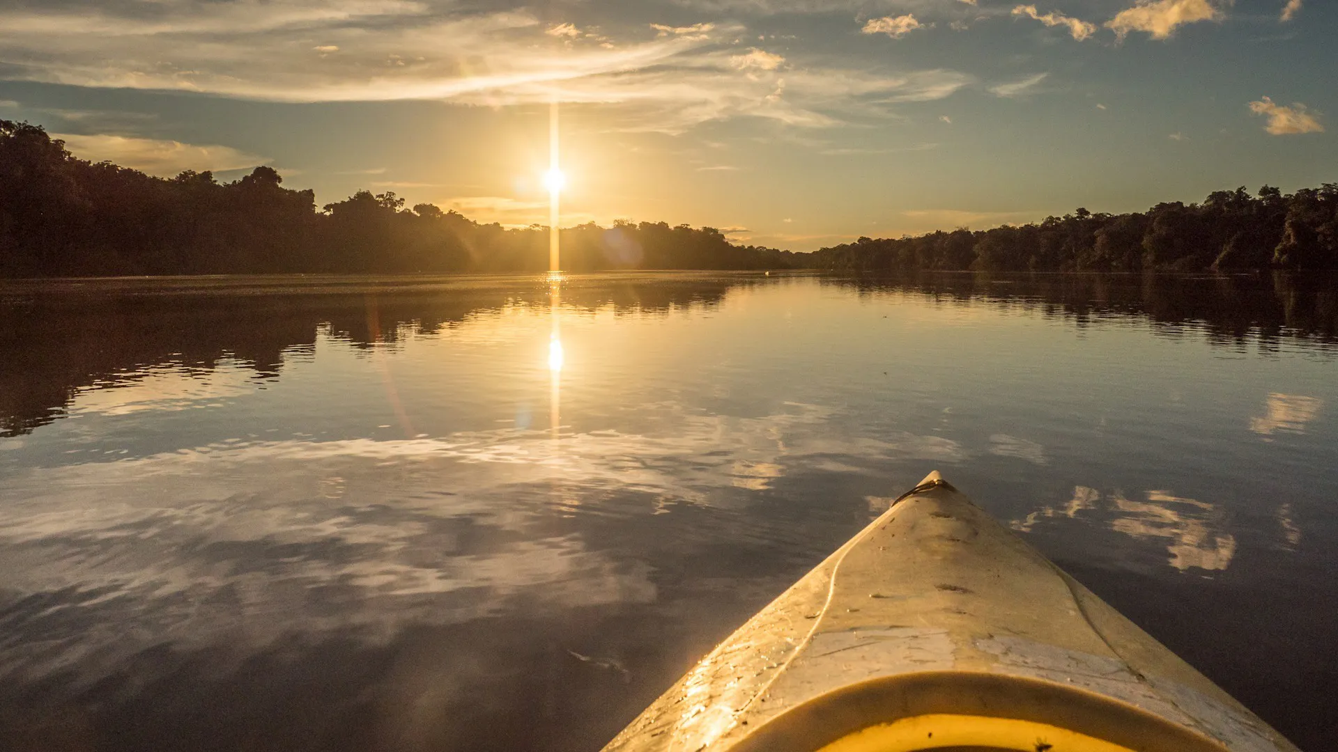 A canoe heads toward a sunset on the Amazon river