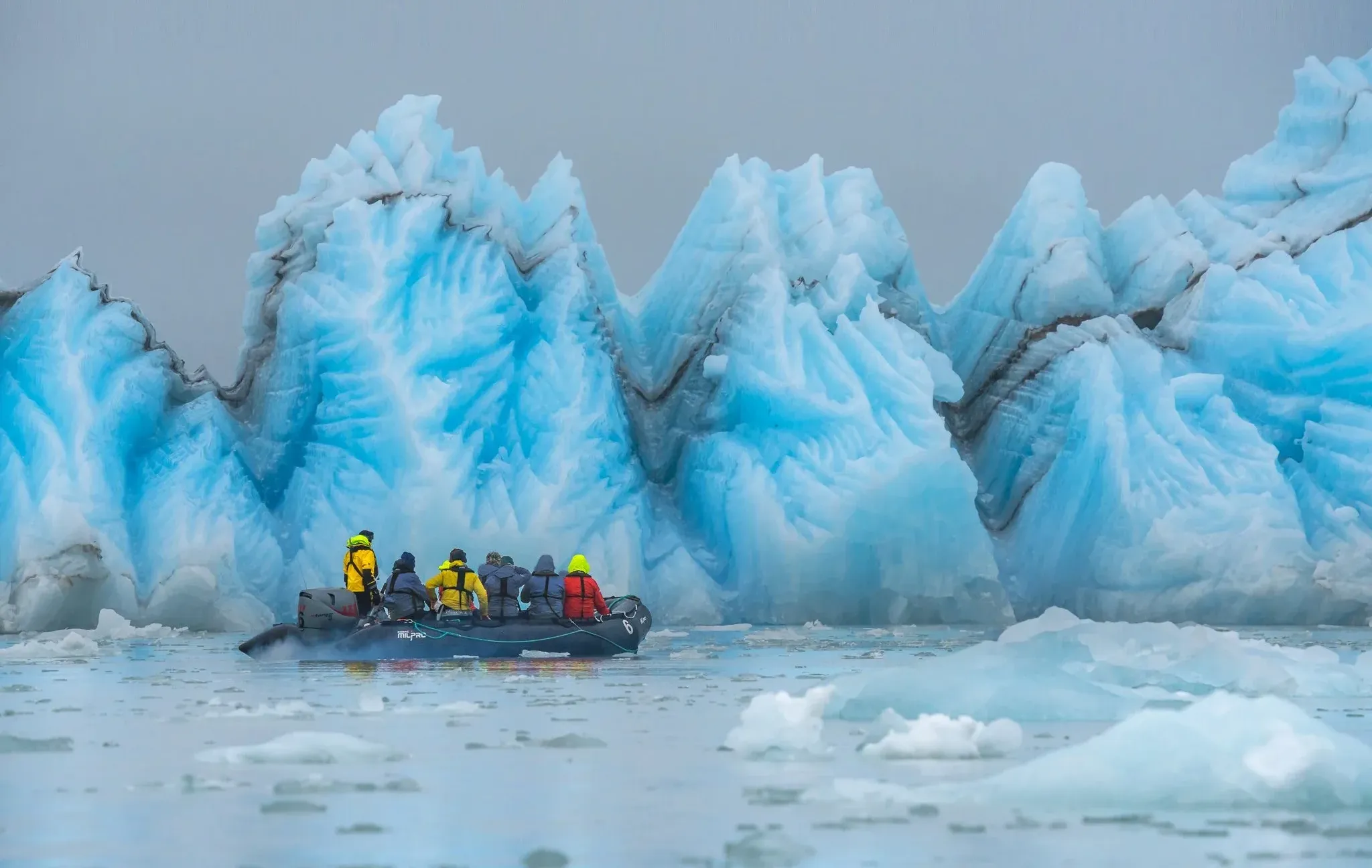 Antarctic explorers ride a zodiac along ice structures