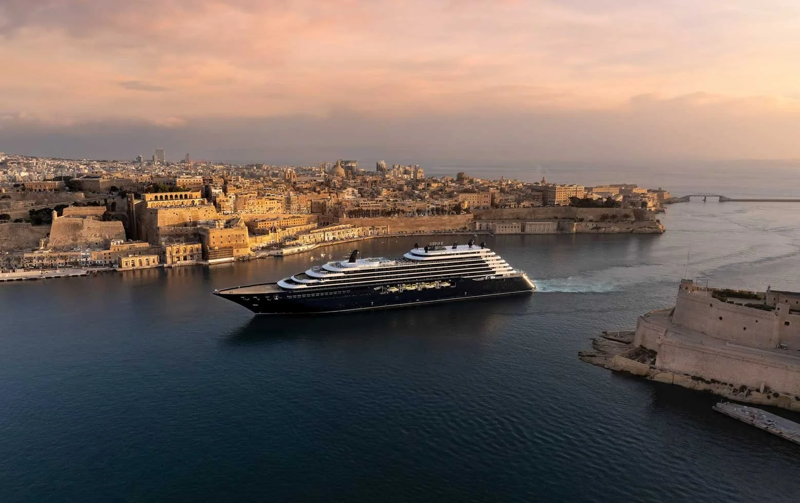 A yacht-like cruise ship sails past a European coastline