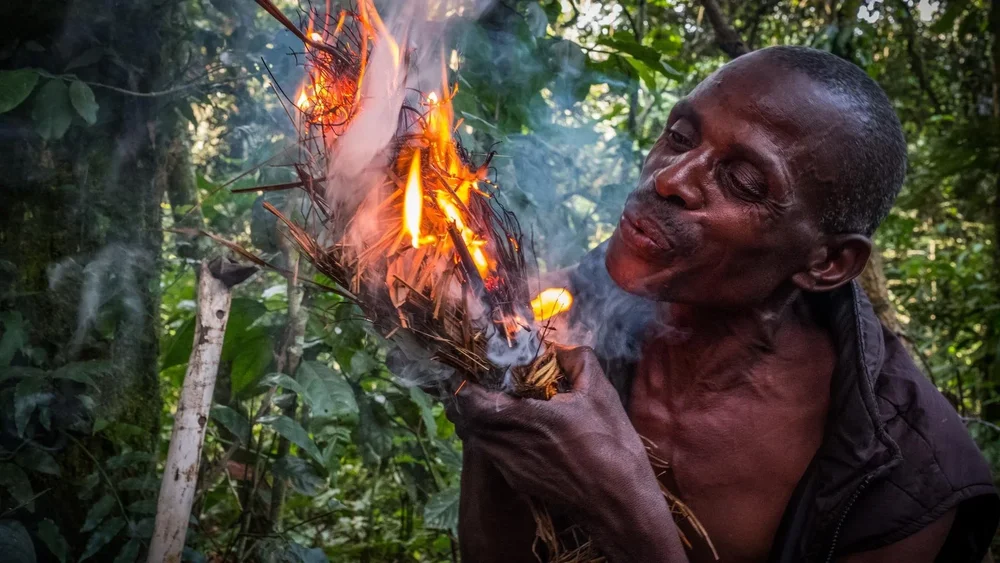 An African tribesman blows on a burning bunch of twigs to start a fire