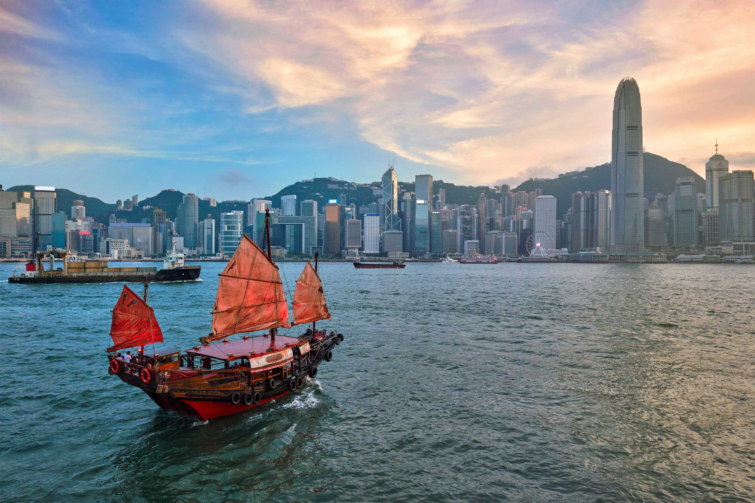 An authentic sailboat sails toward the skyline of Hong Kong