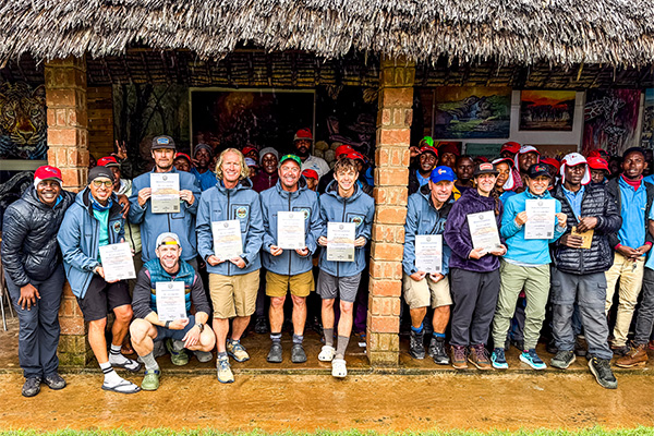 A group poses with certificates under a thatched roof