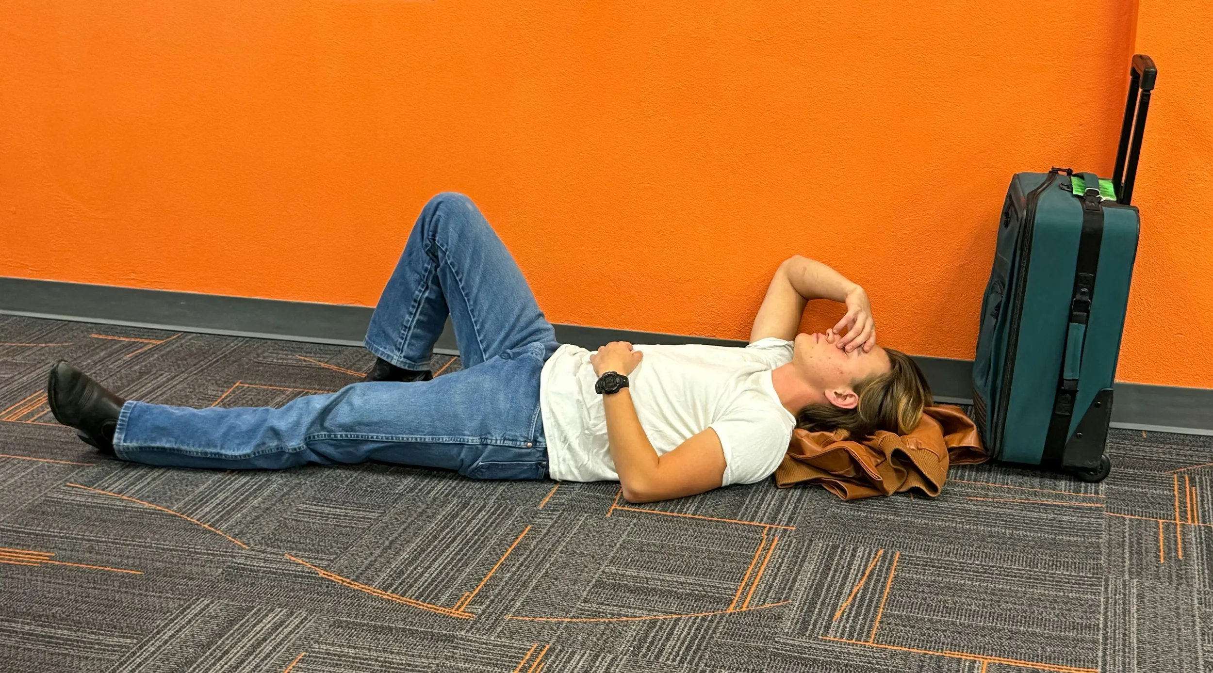 A frustrated traveler lies next to his luggage