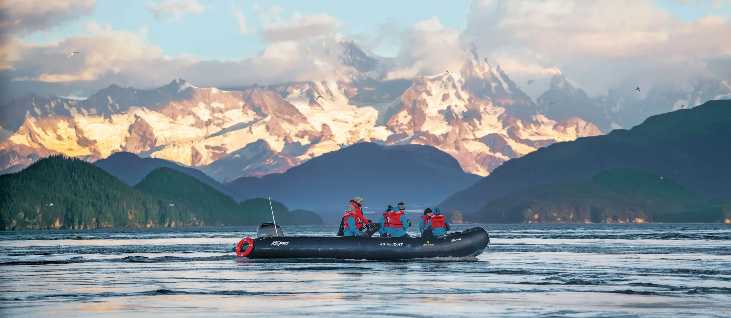 2 zodiacs cruise past a massive mountain range in Alaska