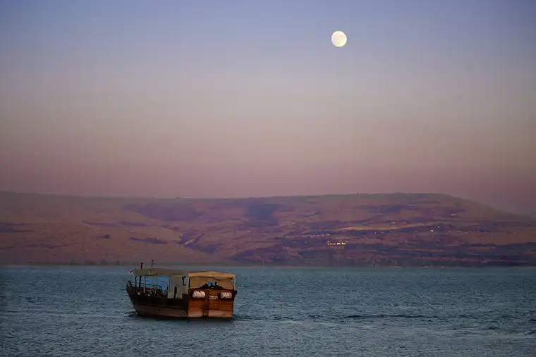 A lone boat travels the Sea of Galilee at sunset