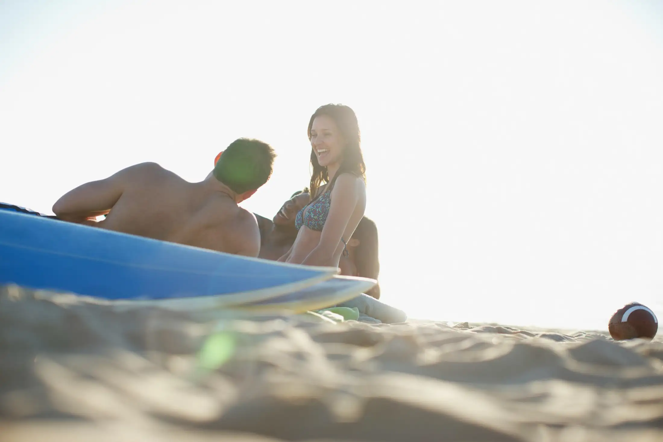 A group of friends laughs on a beach next to surfboards