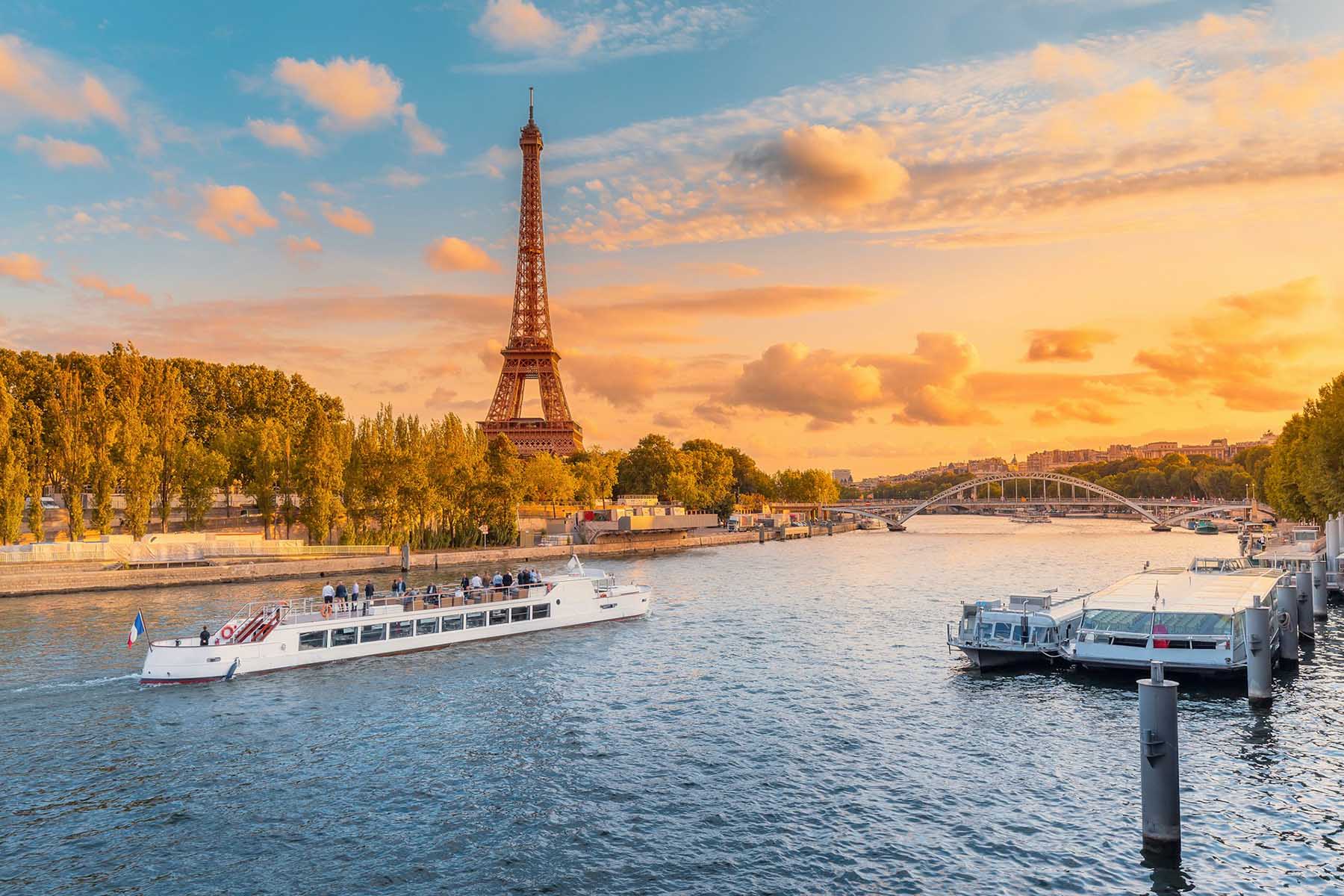 A river cruise ship with the Eiffel Tower in the background at sunset
