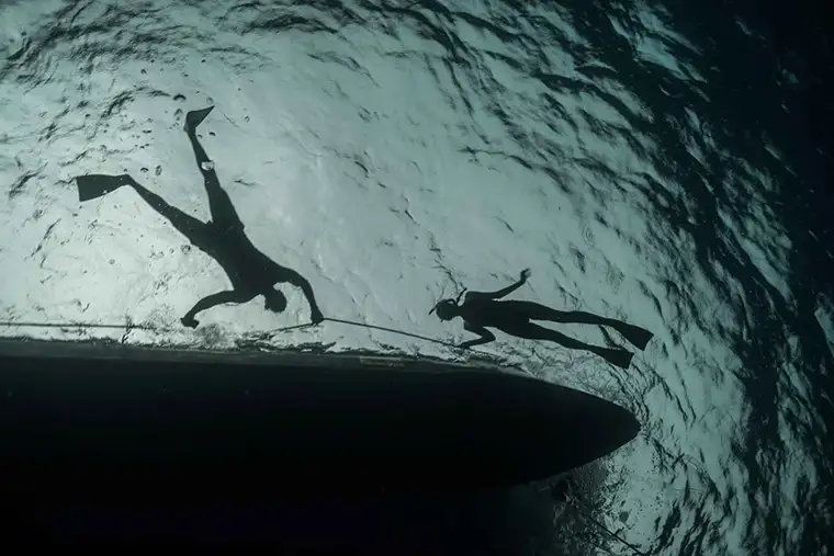 Upward shot of two swimmers hanging onto a boat