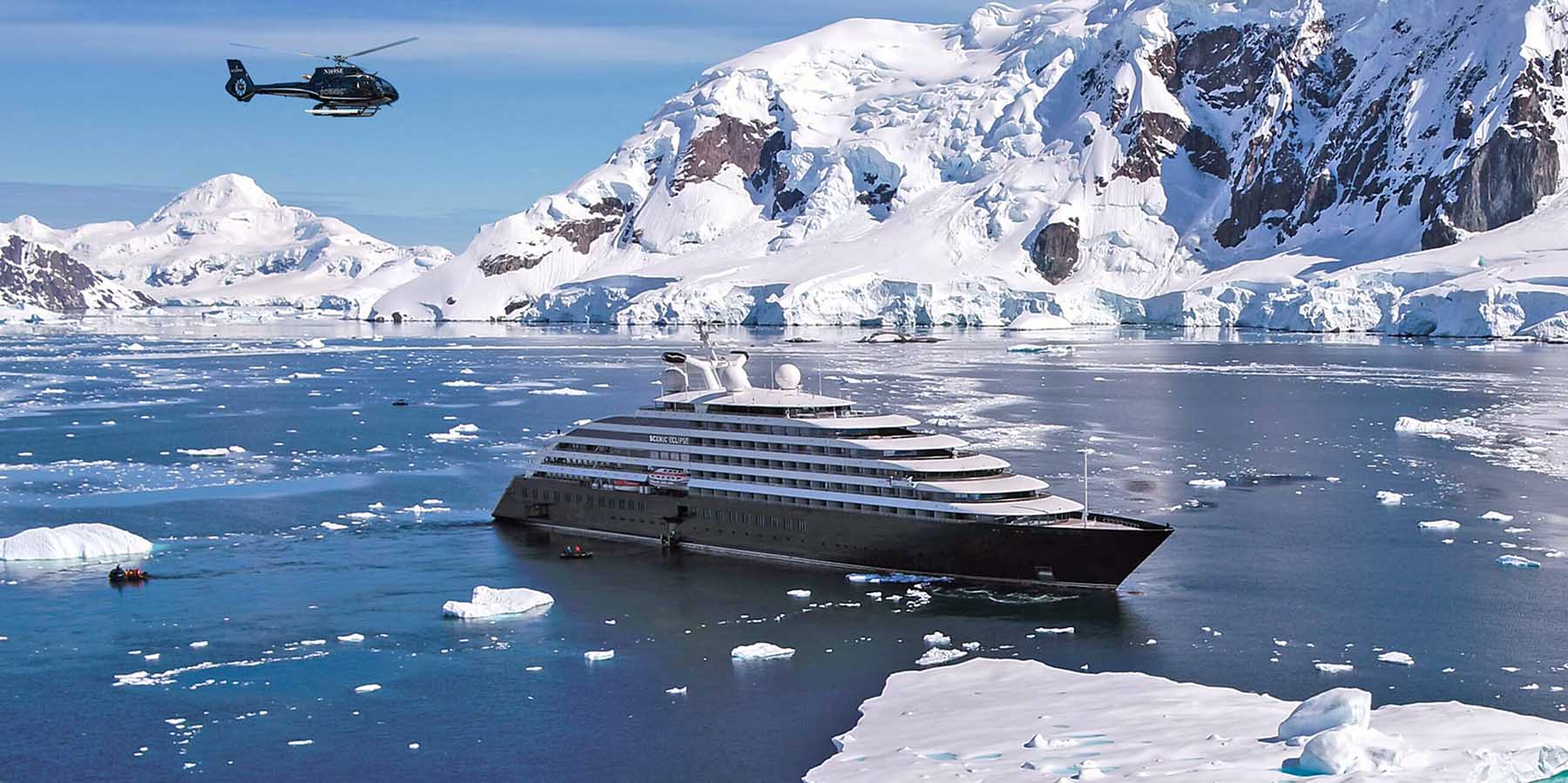 Scenic Eclipse anchored in Antarctica with a helicopter in flight overhead