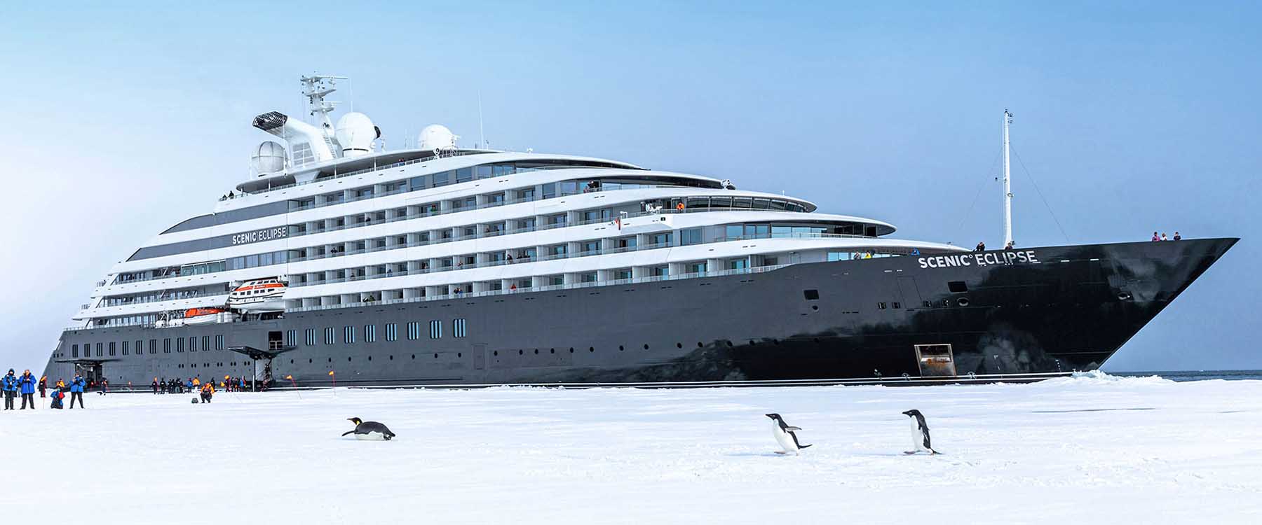 Scenic Eclipse alongside an Antarctic ice sheet with penguins gathered in the foreground