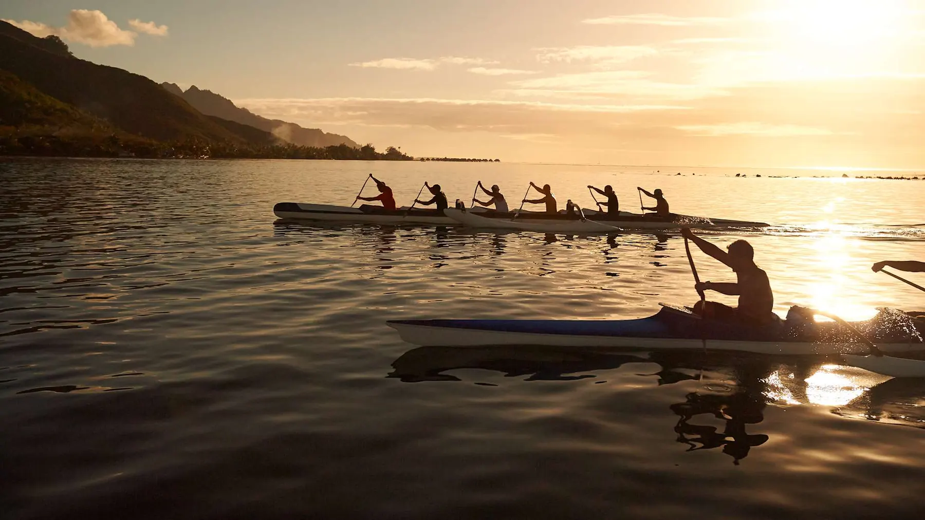 Traditional Tahitian outrigger canoes gliding across a golden sunset lagoon