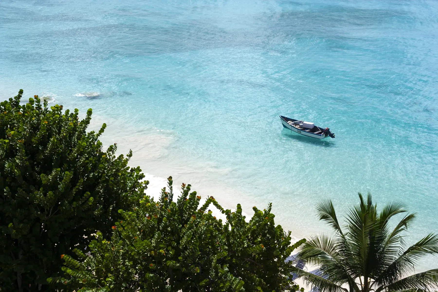 A small boat floats just off a beach in the Caribbean
