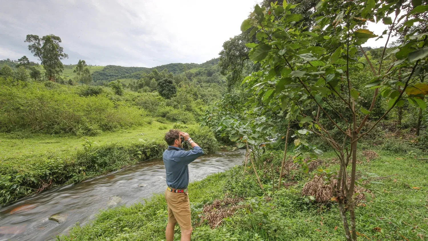 A man bird watches next to a creek and forest