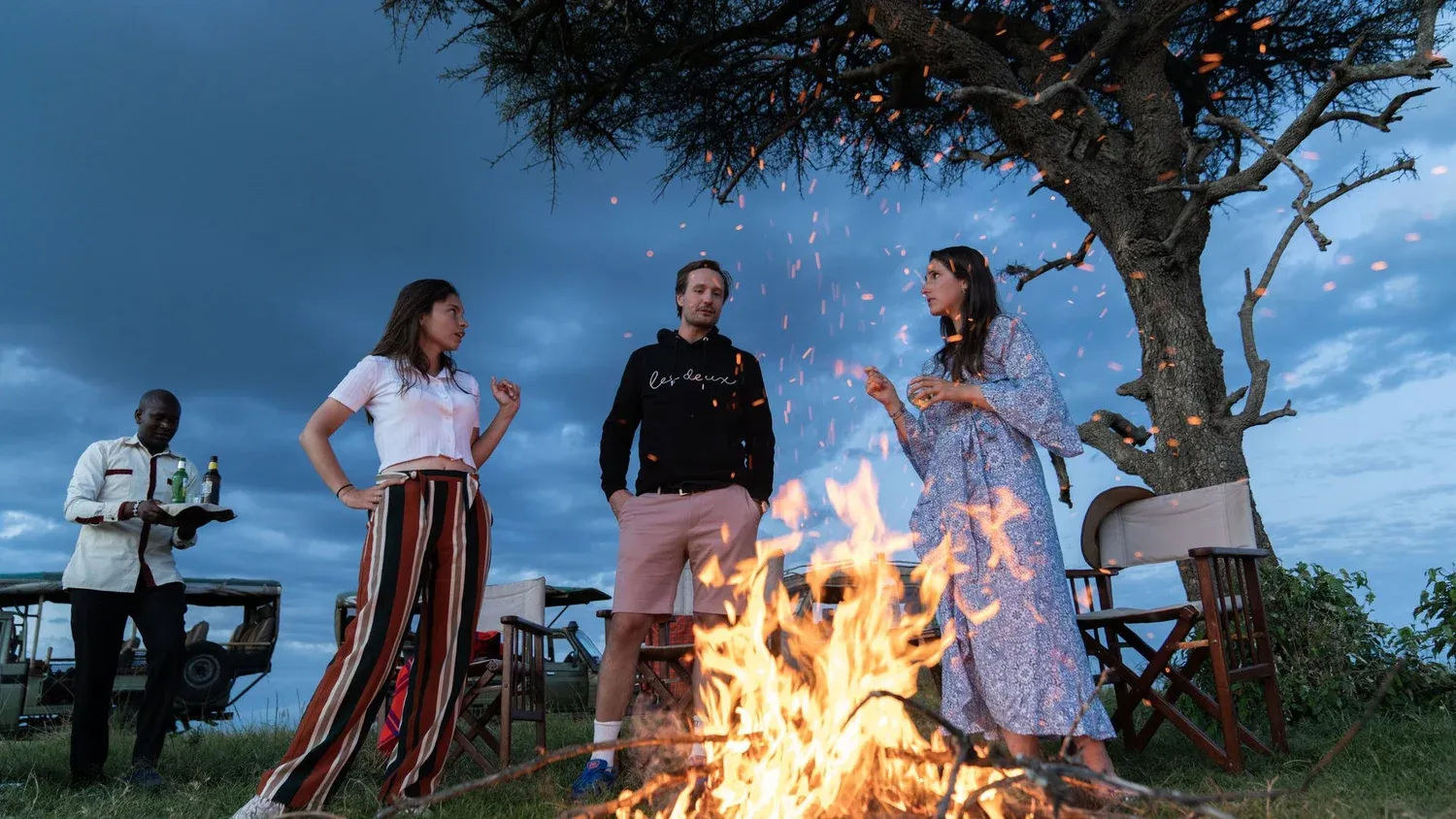 Safari guests stand around a camp fire
