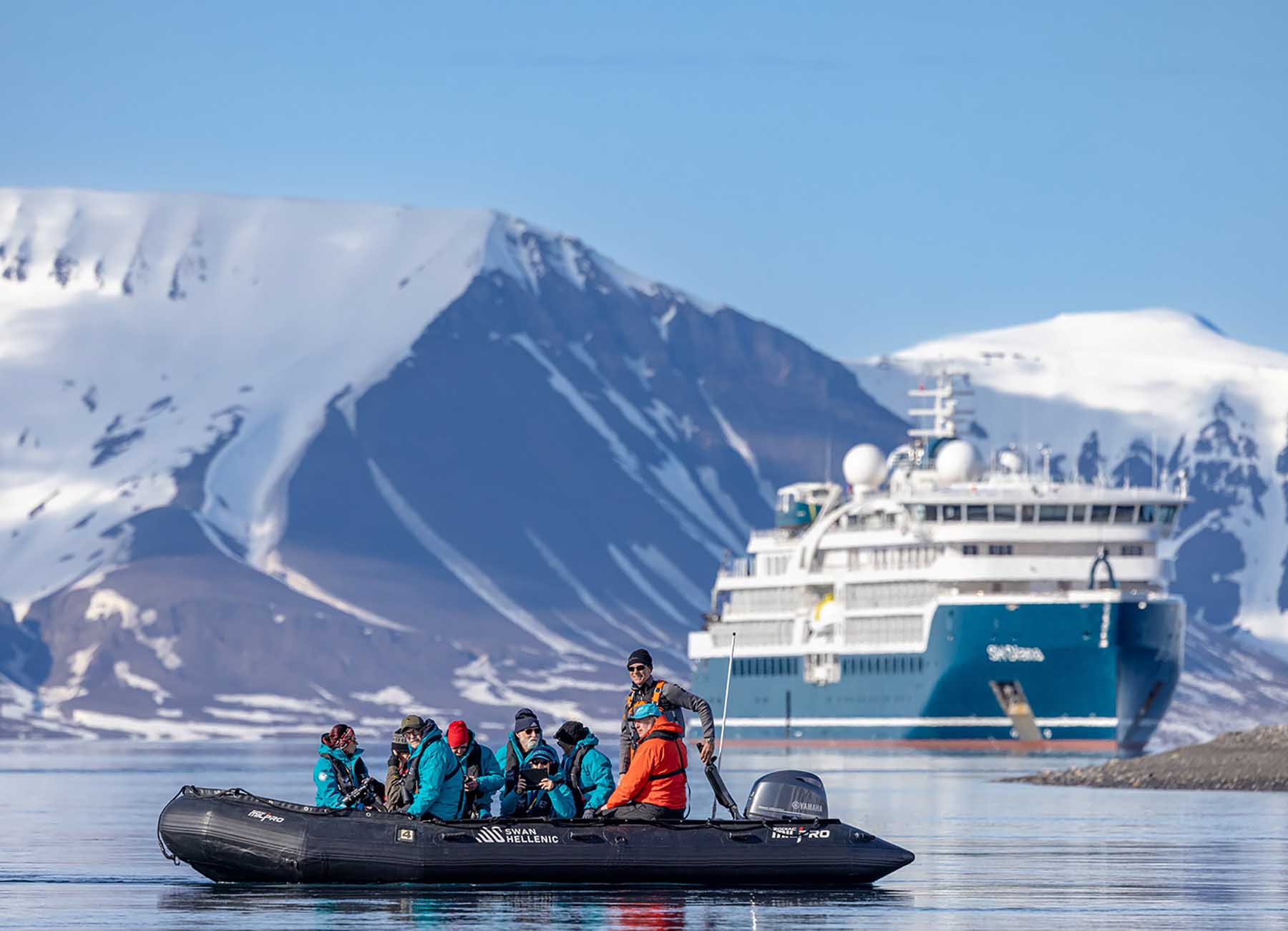 A zodiac full of passengers cruises past a cruise ship in Antarctica