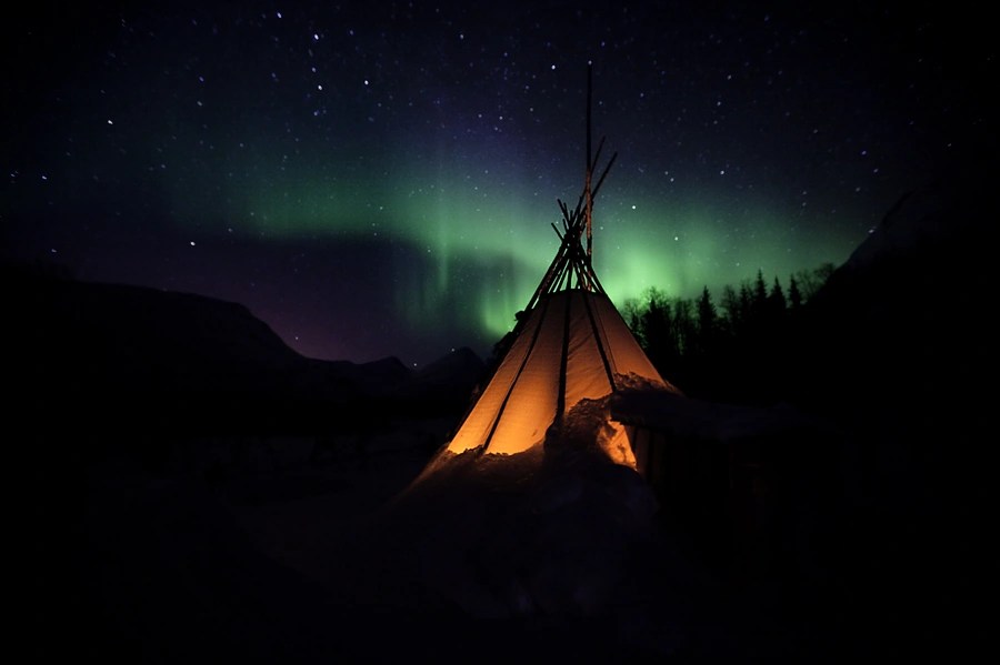 Glowing teepee camp lit from within on an Arctic Norway beach at dusk