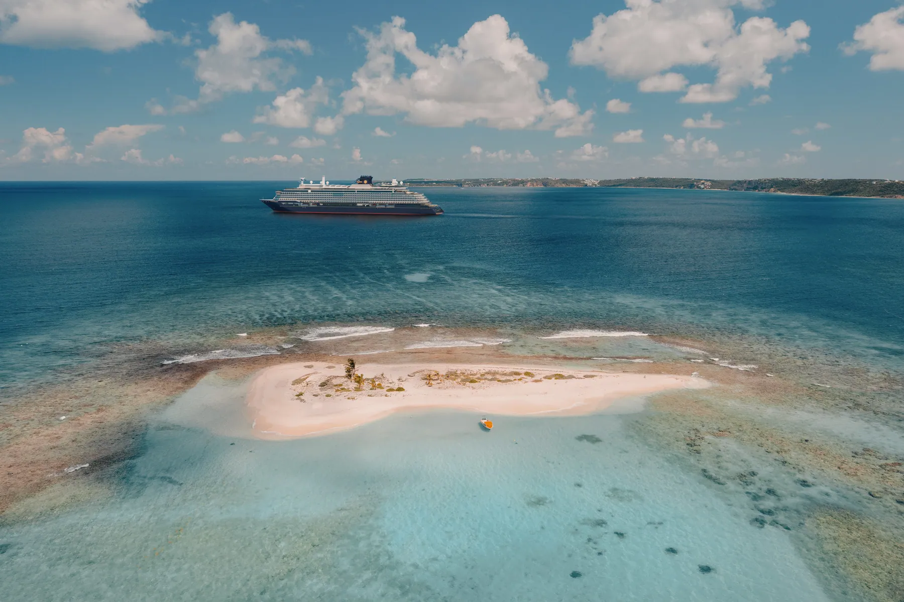 An Explora ship anchored off a small sandbar island ringed by turquoise shallows