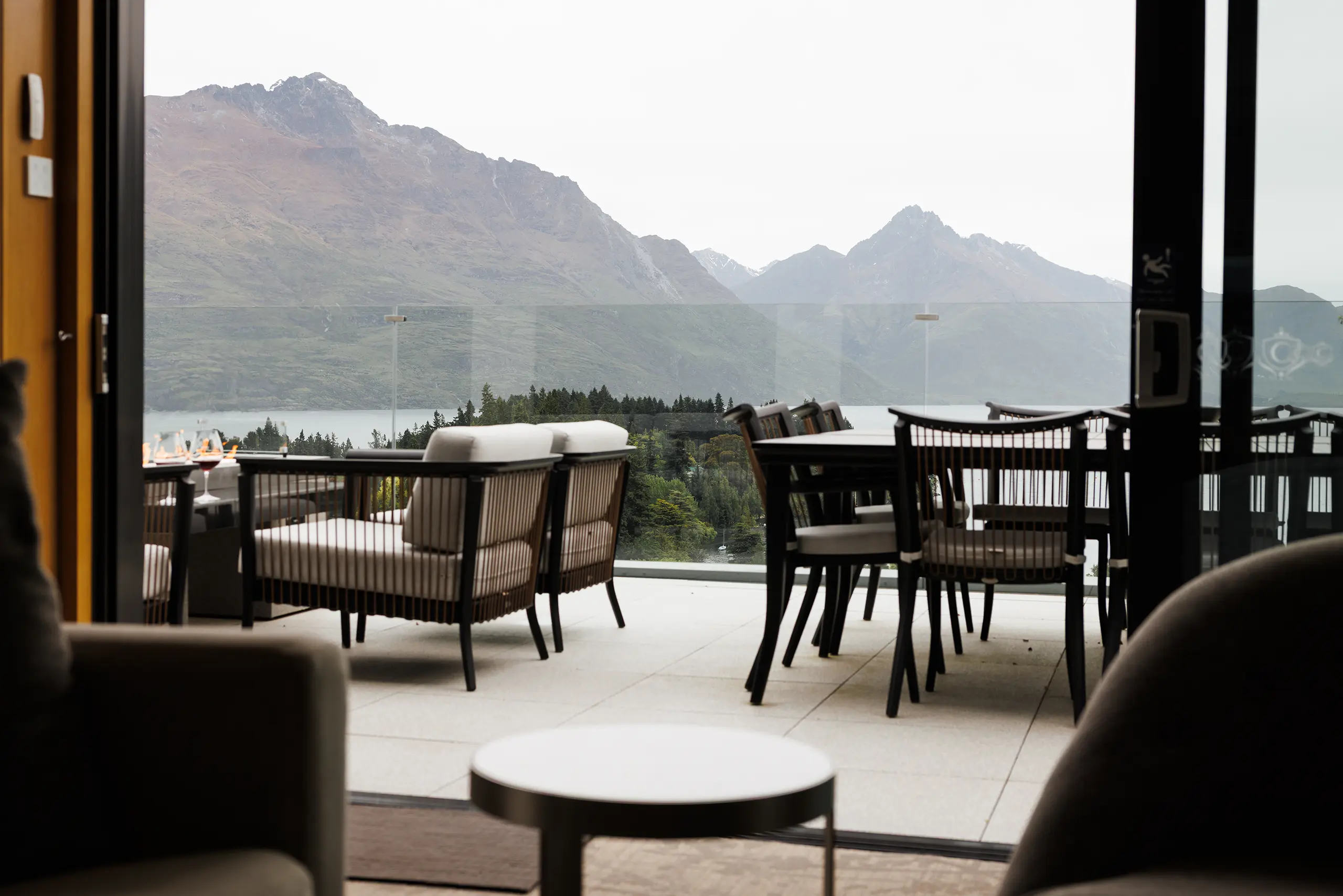 The Carlin Hotel Suites - Outdoor patio with cushioned chairs and dining table overlooking a lake and mountains in the background.