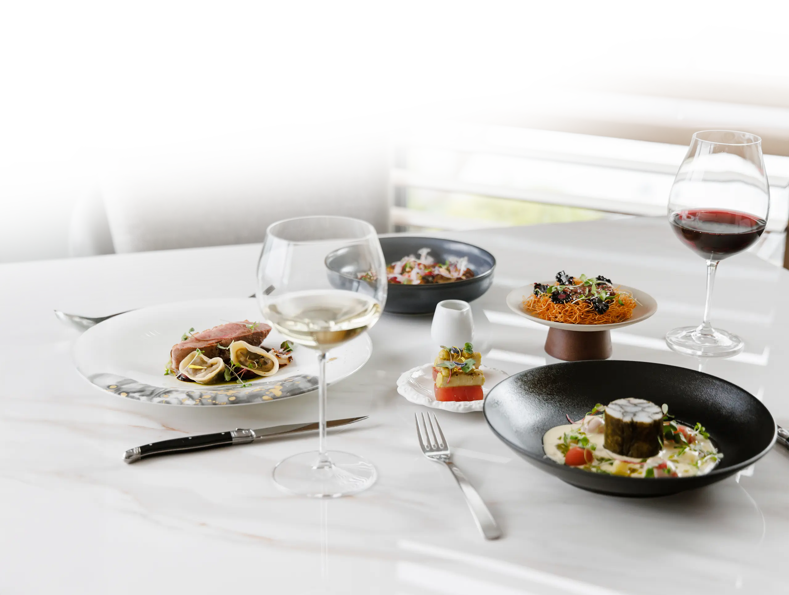 Elegant table setting with gourmet dishes and glasses of red and white wine on a marble surface.