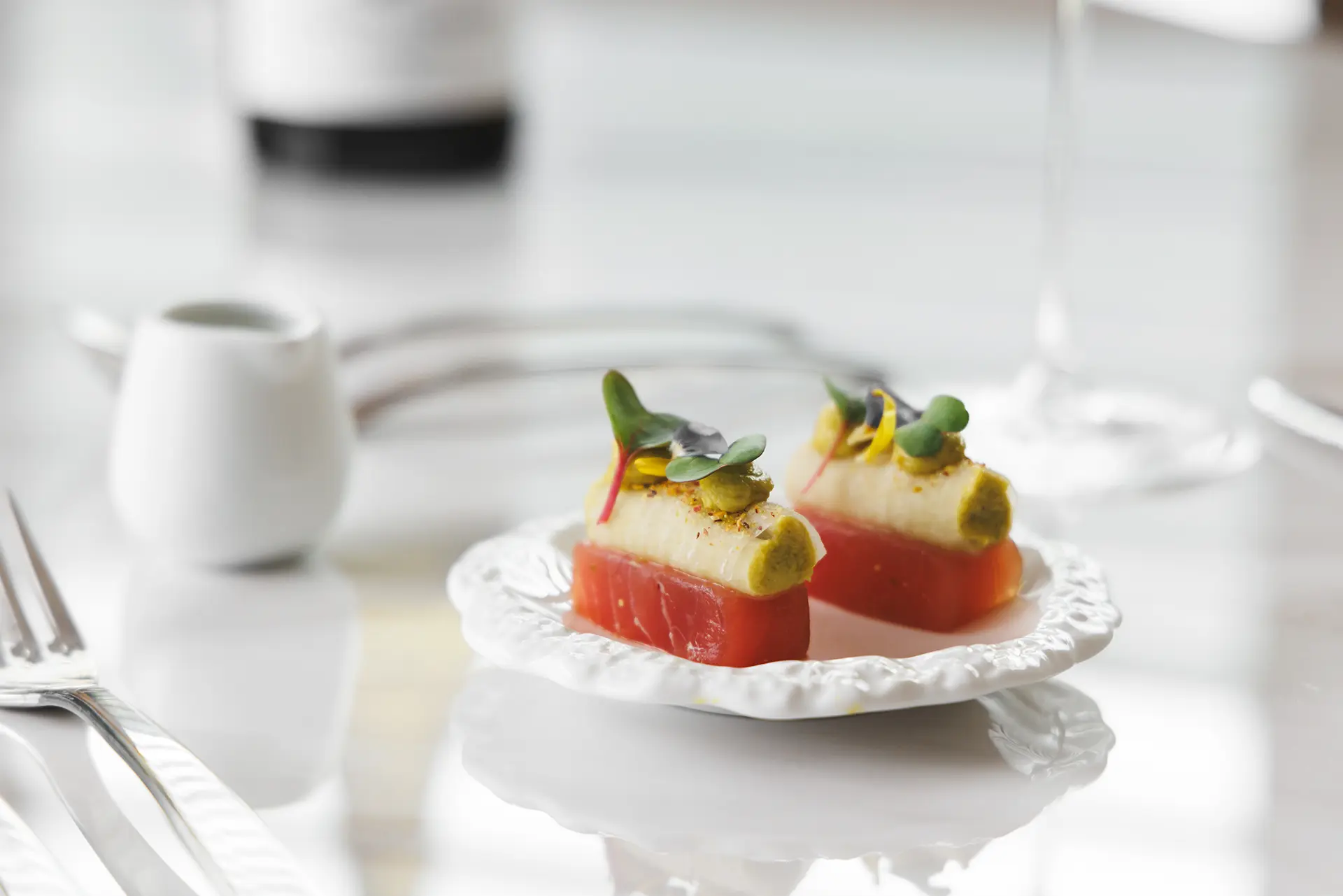 Two elegant appetizers with a red base topped with a creamy white layer and garnished with microgreens on a white plate.