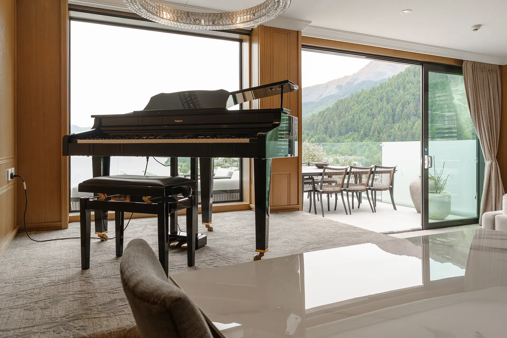 Modern room with a black grand piano, large windows, and a balcony overlooking green forested mountains.