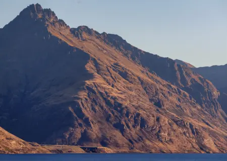 The Carlin - Sunlit rocky mountain with rugged slopes under a clear blue sky.