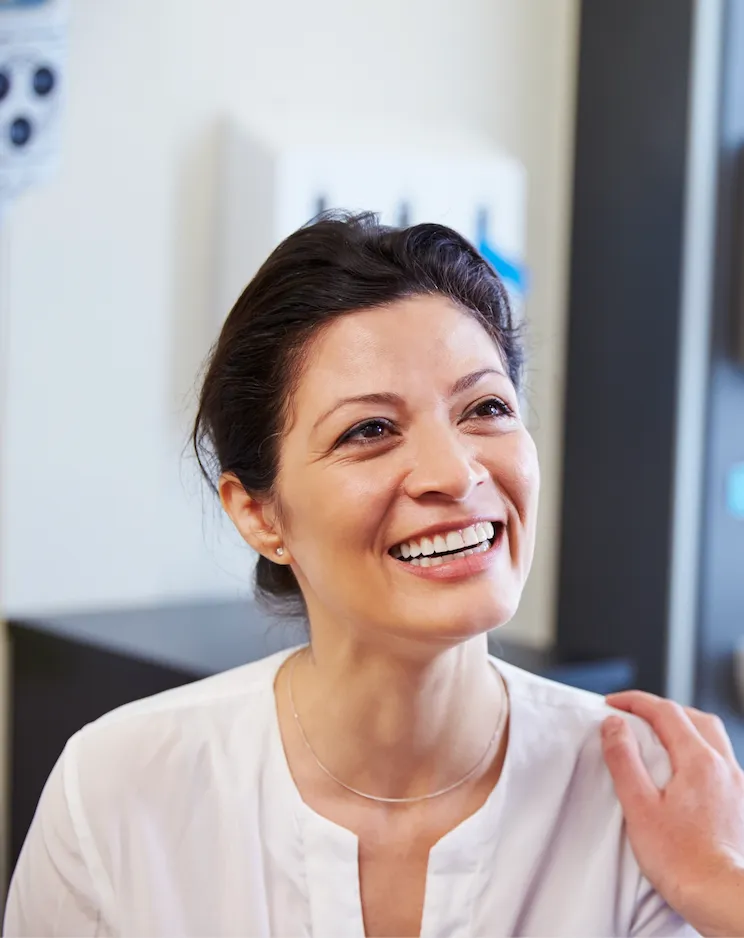 Confident middle-aged woman smiling happily after dental implant treatment, showcasing natural-looking teeth, restored confidence, and joyful expression in a modern dental office.