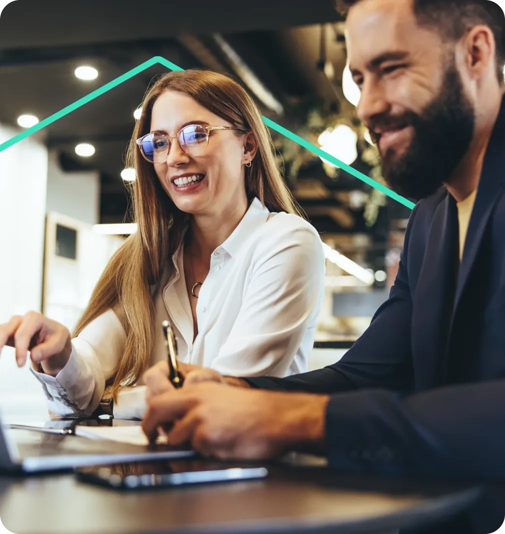 Two happy real estate agents discussing work at a desk with a laptop and documents.