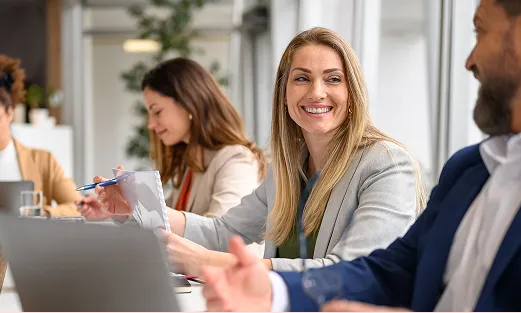 Smiling woman in business attire engaging in conversation with a colleague in a modern office setting.