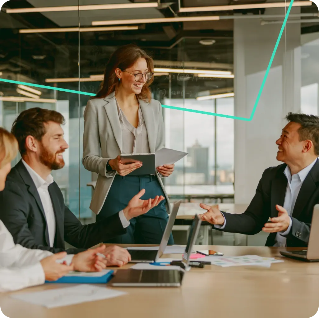 Businesswoman standing and presenting to colleagues in a modern office meeting room.