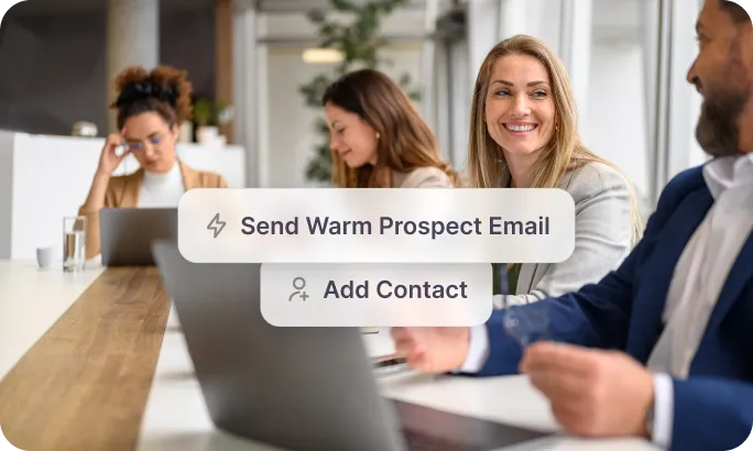 Four professionals sitting at a long table with laptops, two chat bubbles showing 'Send Warm Prospect Email' and 'Add Contact'.
