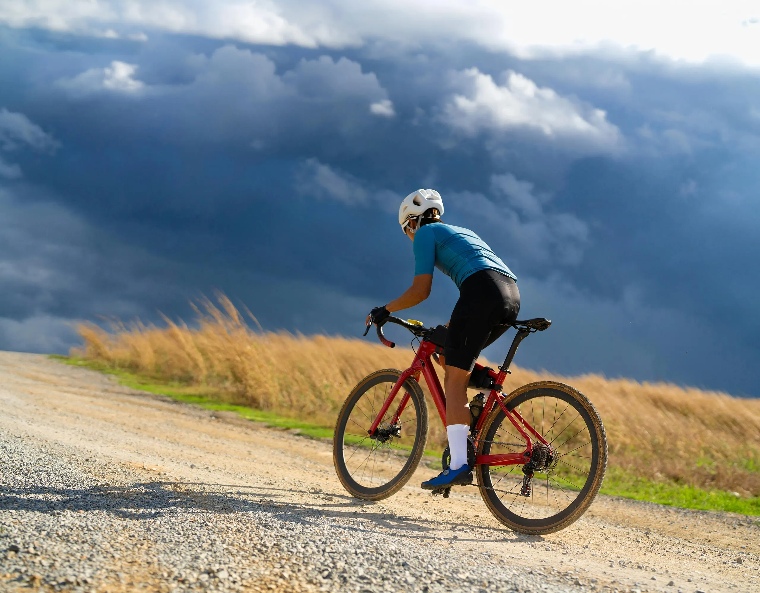 Cyclist wearing a helmet and black cycling kit, sitting on a red and black road bike against a dramatic cloudy sunset sky.