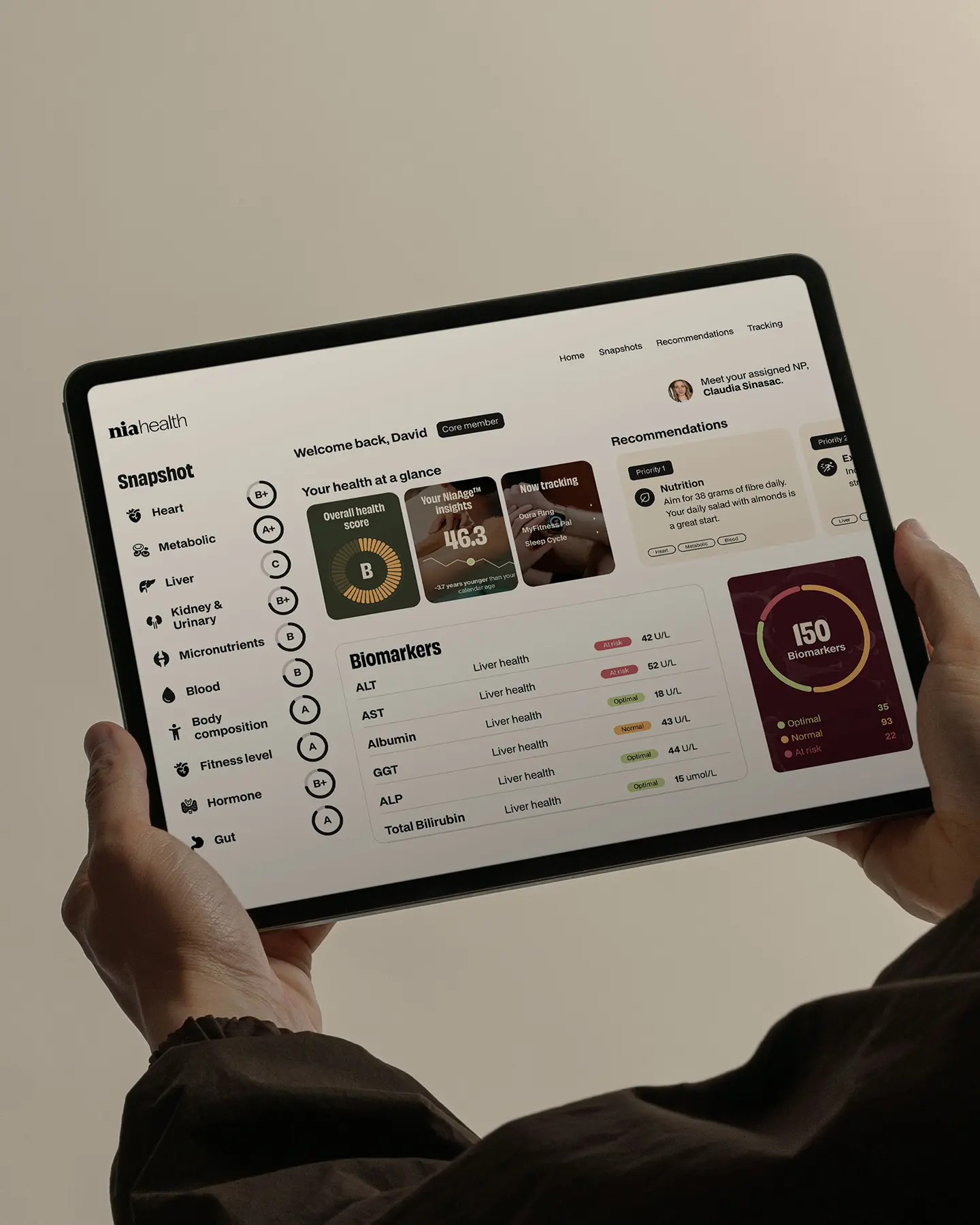 Person holding a tablet displaying a health dashboard with sections for snapshot, health score, biomarkers, and recommendations.
