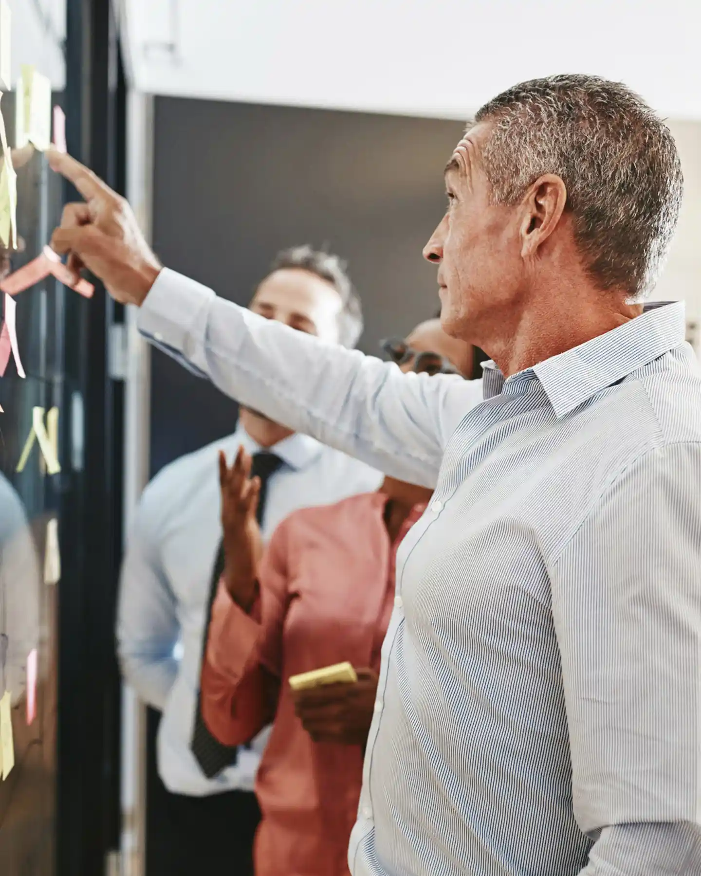 Three professionals collaborating and placing sticky notes on a glass wall during a brainstorming session.