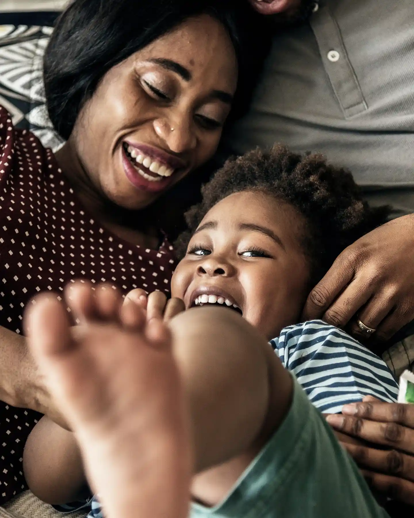 Smiling mother lying down and playing with her laughing child whose foot is in the foreground.