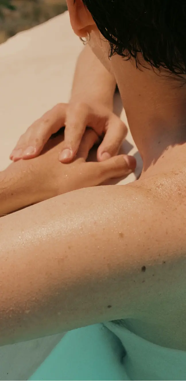 Close-up of a person with wet skin leaning on the edge of a pool with hands clasped.