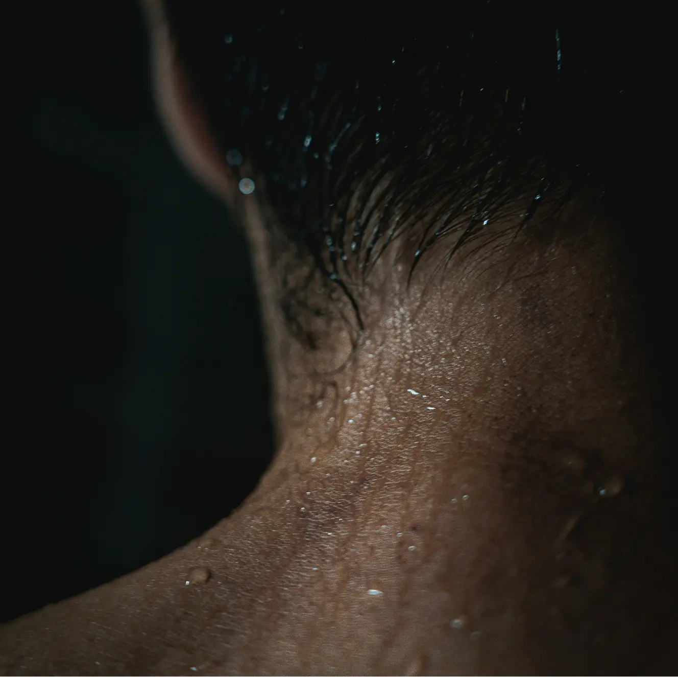 Close-up of a person's wet neck and hair with water droplets against a dark background.