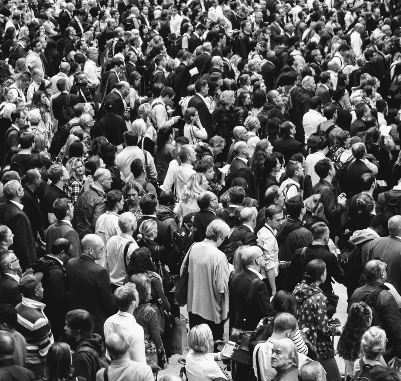 Black and white photo of a large crowd of people standing closely together, mostly looking in the same direction.