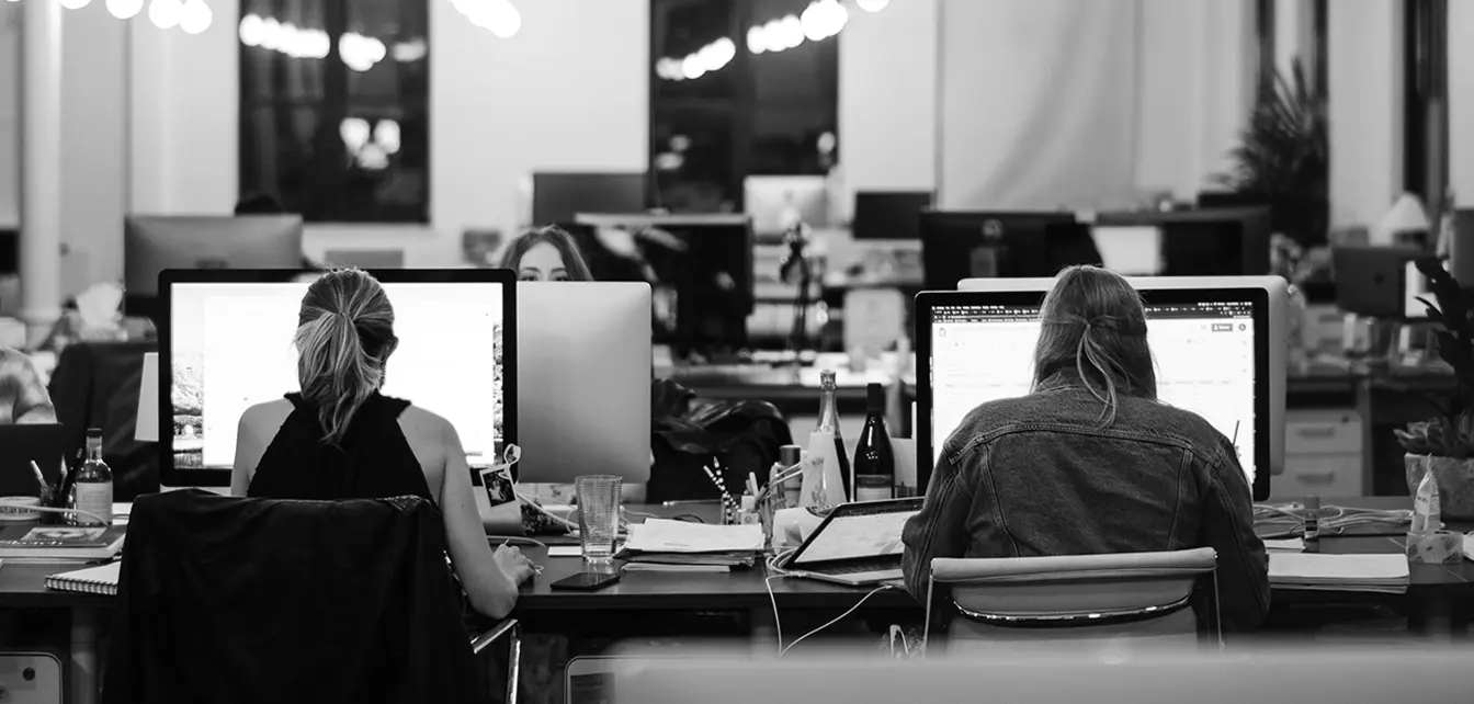 Two women working at desks with computers in a modern open office space.