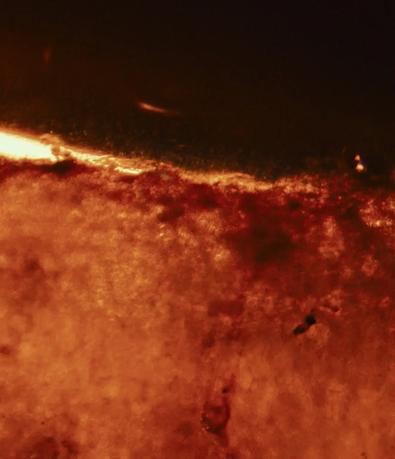 Close-up texture of a reddish-brown surface with a glowing bright edge against a dark background.