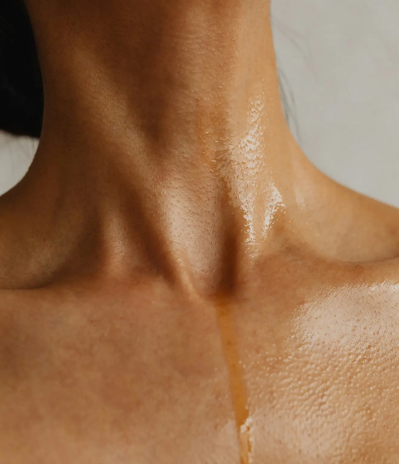 Close-up of a person's neck and upper chest with shiny, moisturized skin.