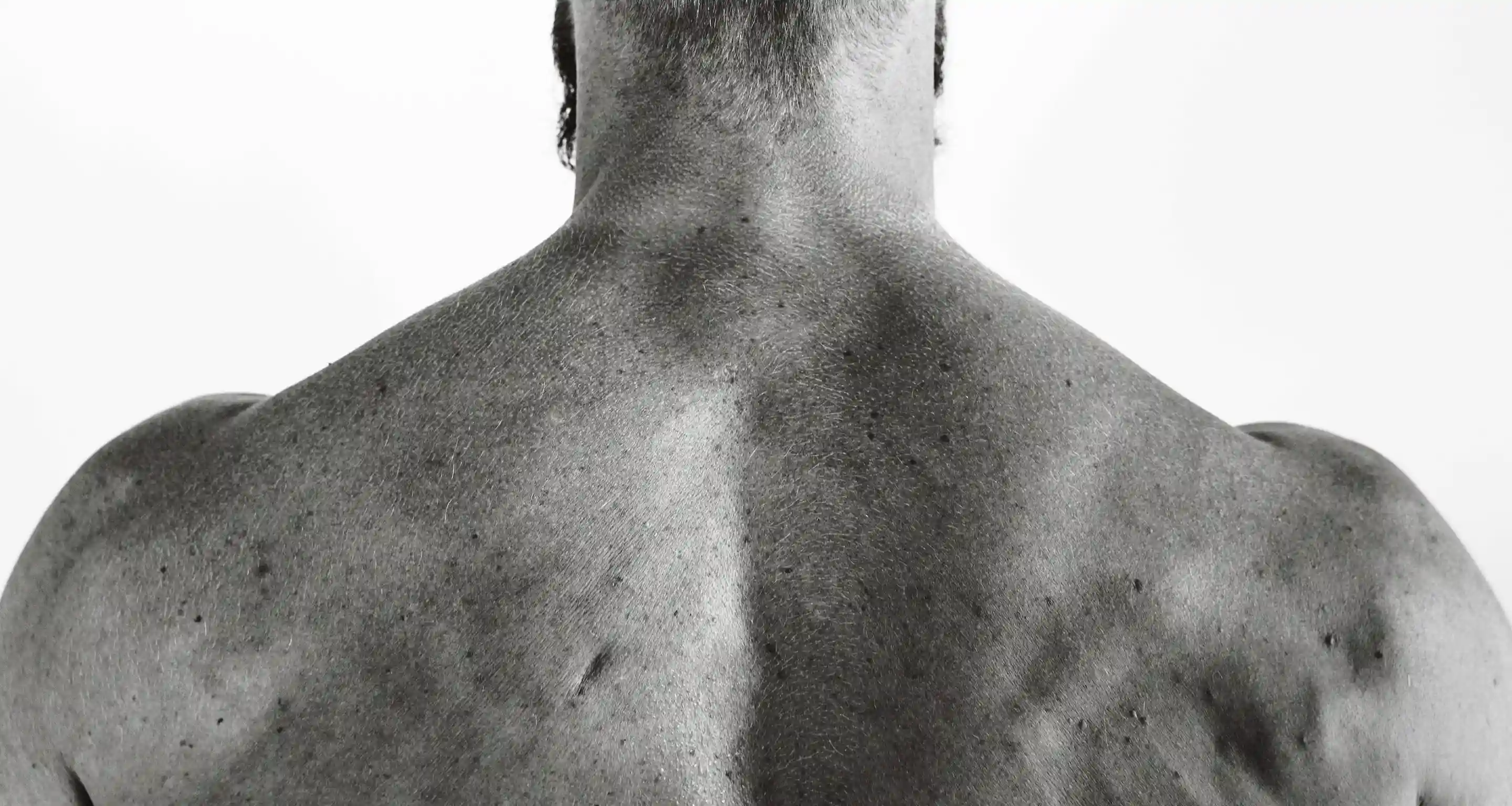 Black and white close-up of a muscular man's back and shoulders.
