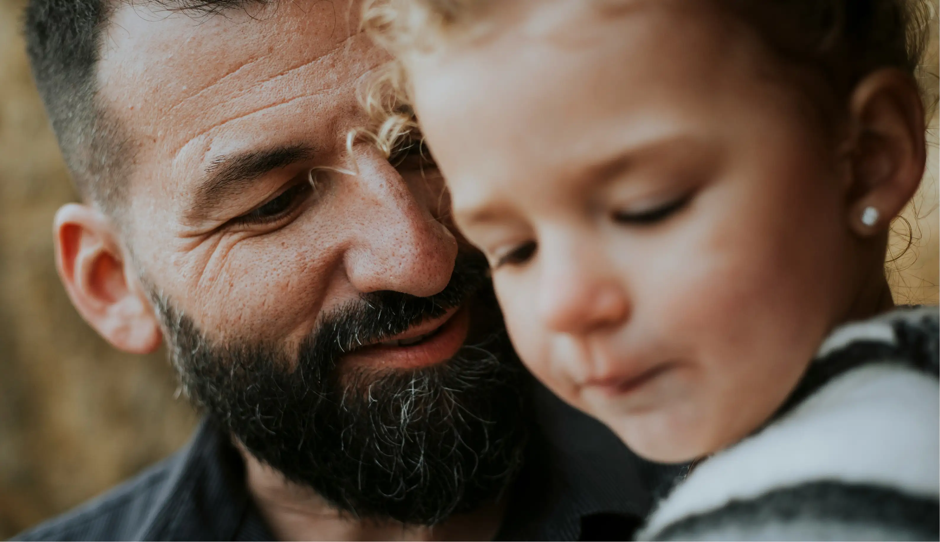 Close-up of a bearded man smiling at a young child with curly hair and an earring.