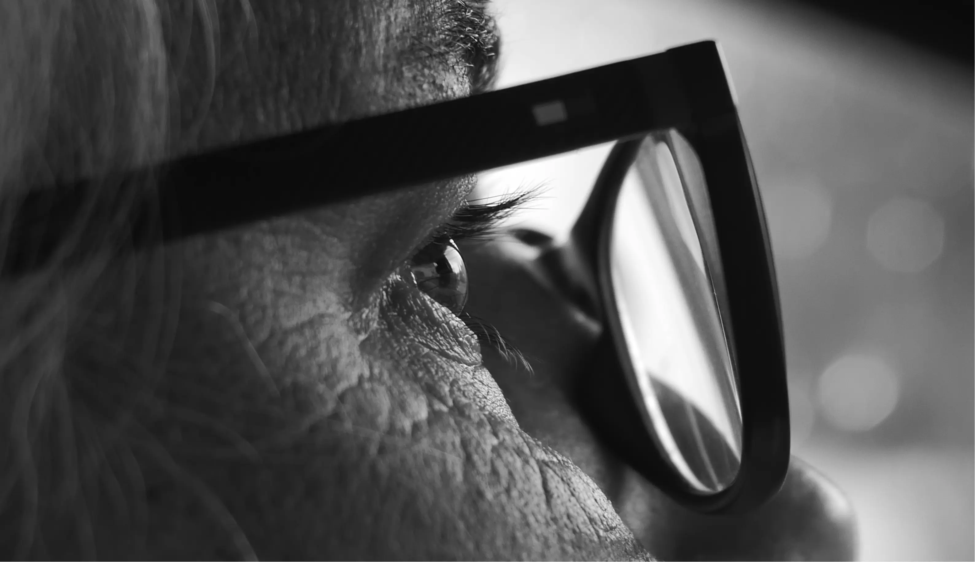 Close-up black and white photo of an eye with glasses reflecting light.