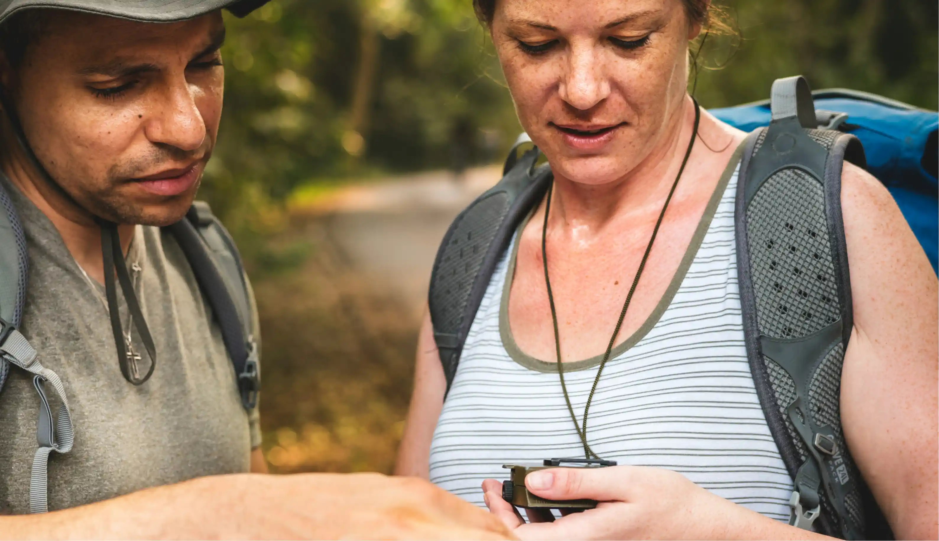 Two hikers with backpacks studying a compass together on a forest trail.