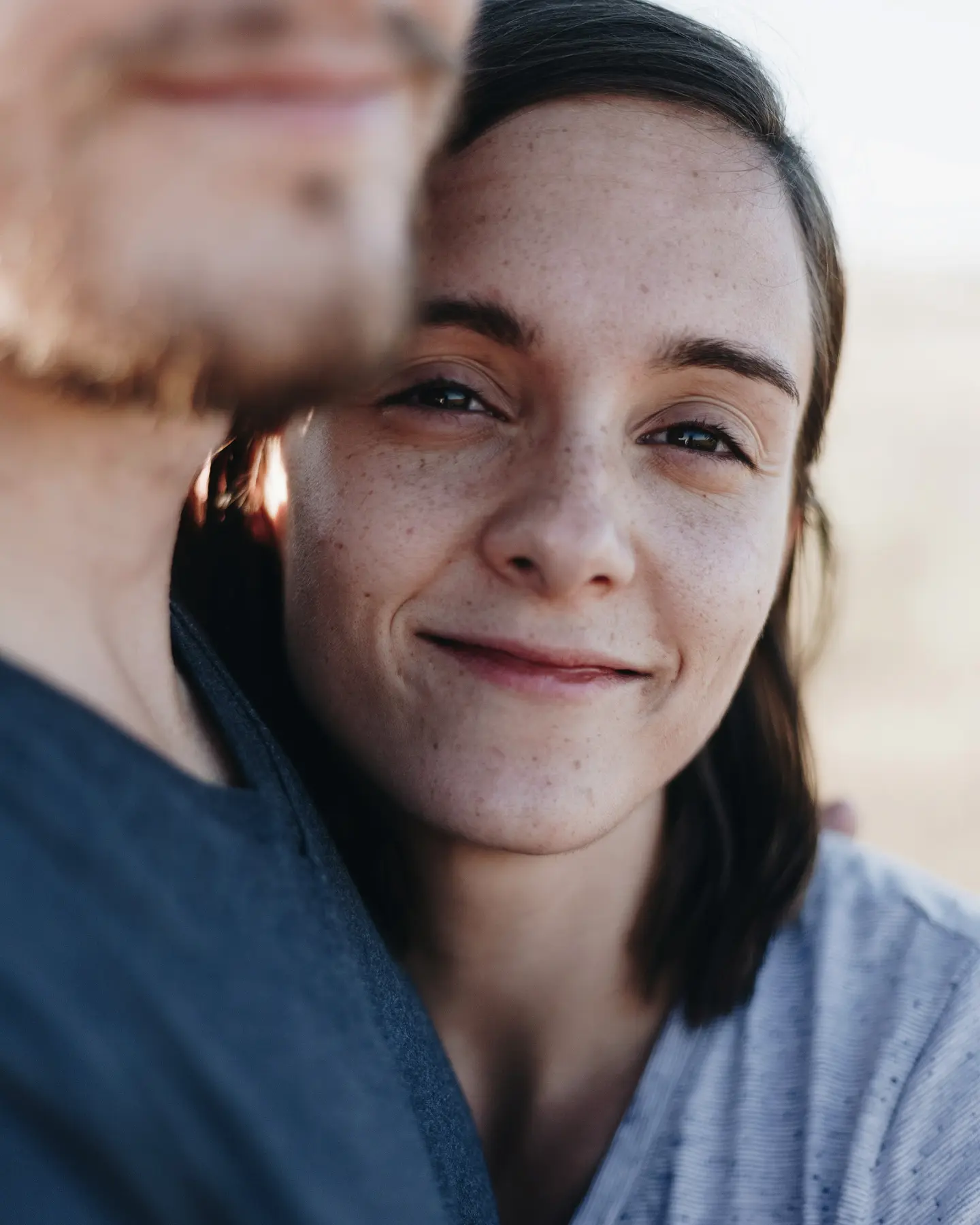 Close-up of a woman with freckles smiling gently while leaning on a man's shoulder.